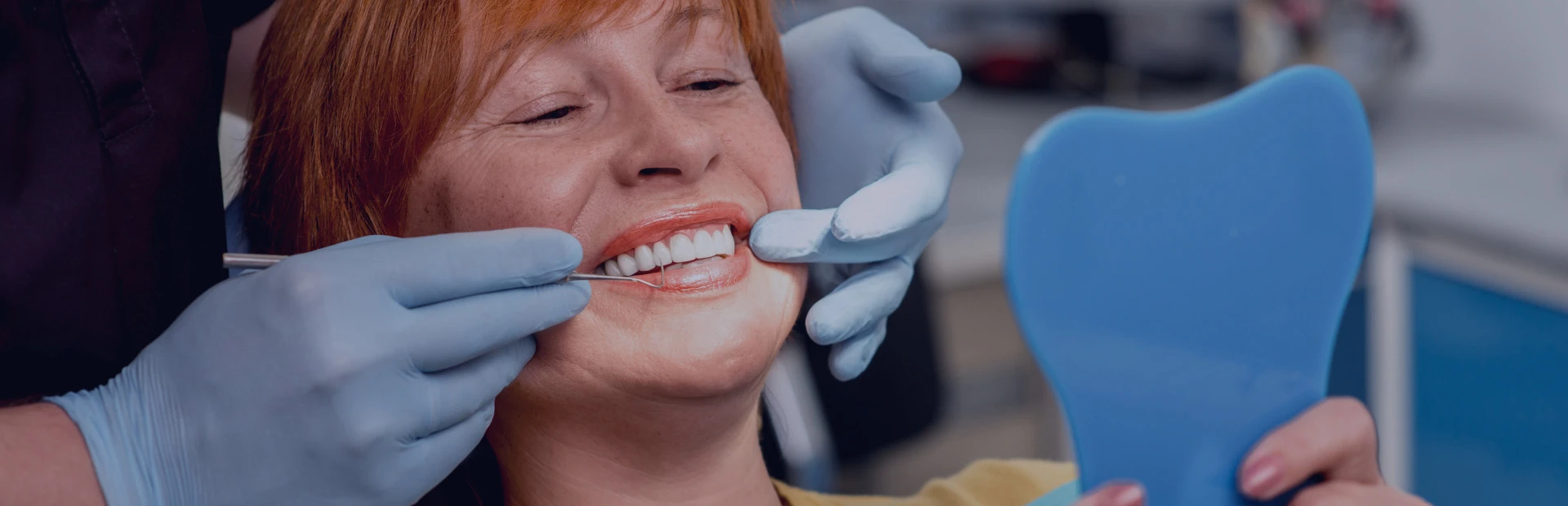 A woman in her 60s is in the dentist's chair smiling, because she knows the correct cleaning and maintenance procedure for her dentures.