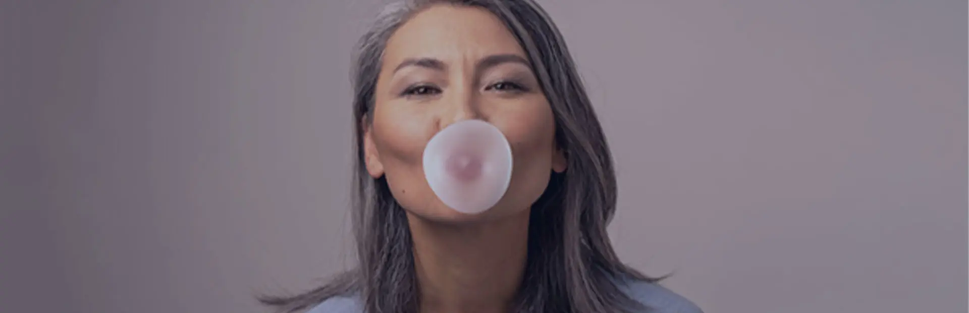 A woman in her 50s blows some bubble gum, as she knows she can still chew gum with dentures while using Fixodent. 