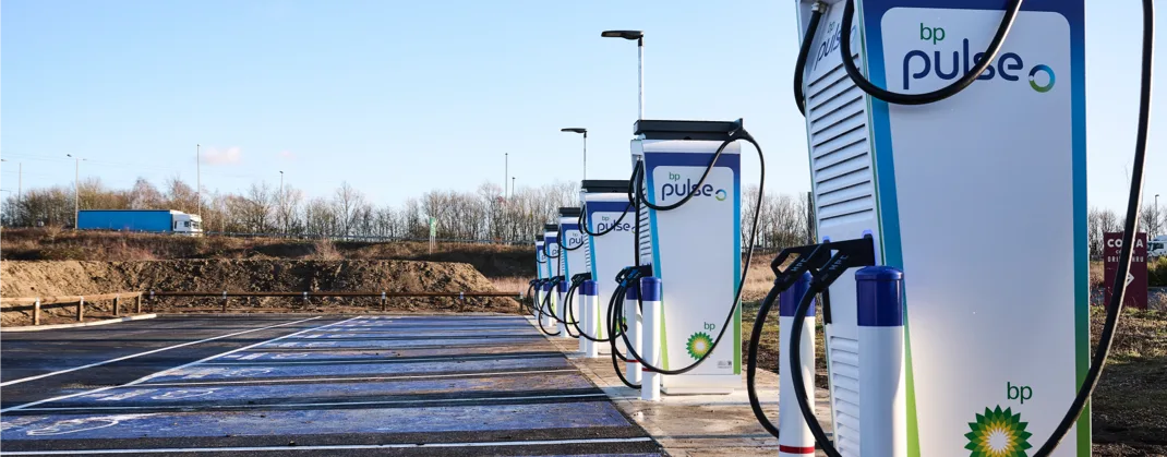 A row of bp pulse ev chargers at a station and a truck driving past in the background on a sunny day.
