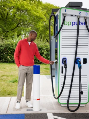 A man wearing a red jumper and beige trousers standing infront of a bp pulse charger and tapping his card on the reader.