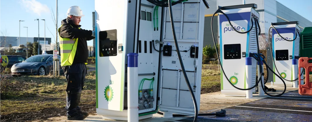 A technician working on a bp pulse EV charger at a station on a bright sunny day.