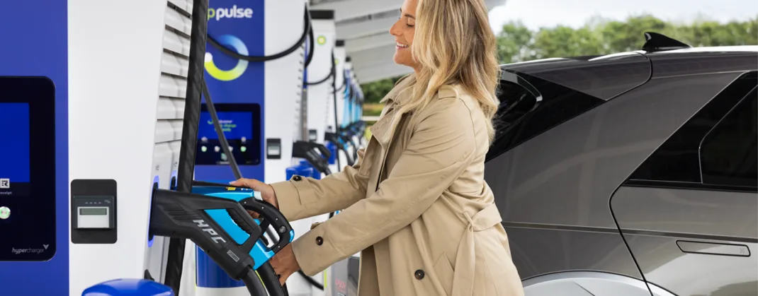A woman at an ev charging station, holding a bp pulse charger, about to charge her EV.