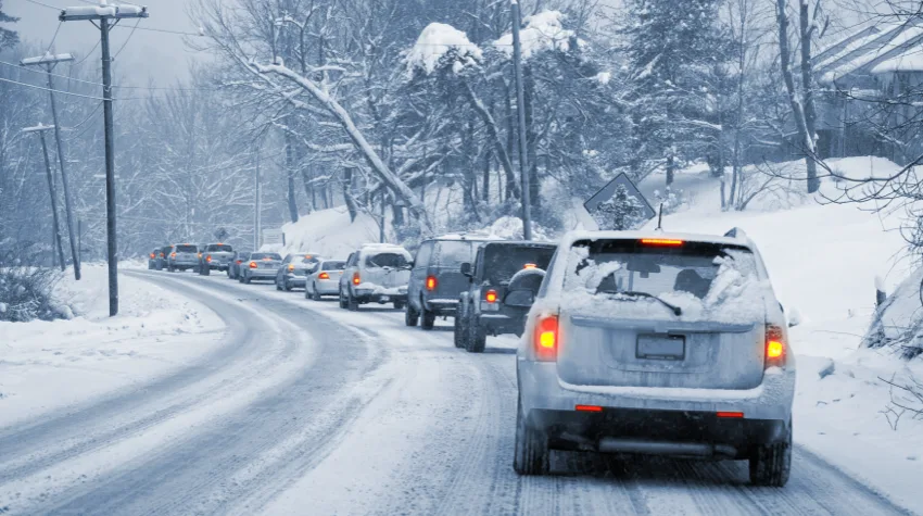 Cars stationary in traffic on a snowy road, surrounded my snow covered trees.