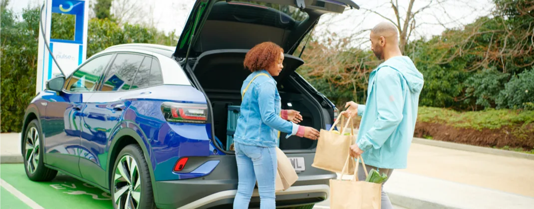 A couple returns from a shopping trip and loads groceries into their electric vehicle while it charges at a bp pulse charger.