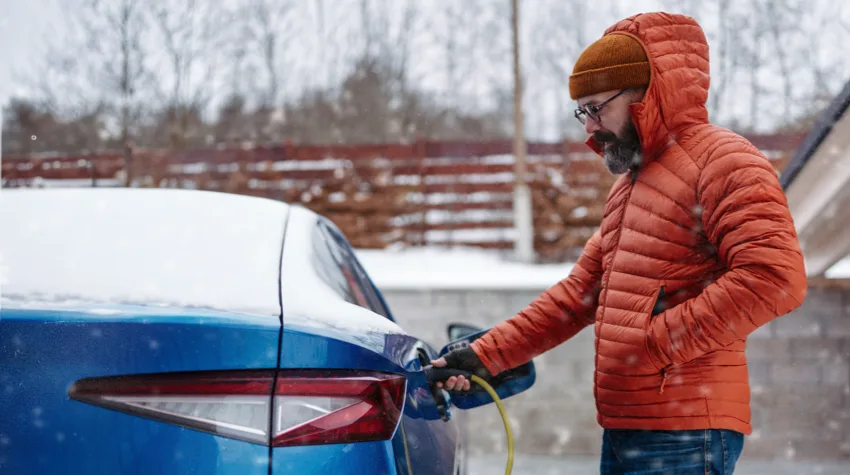 A man in winter jacket is charging his electric car.