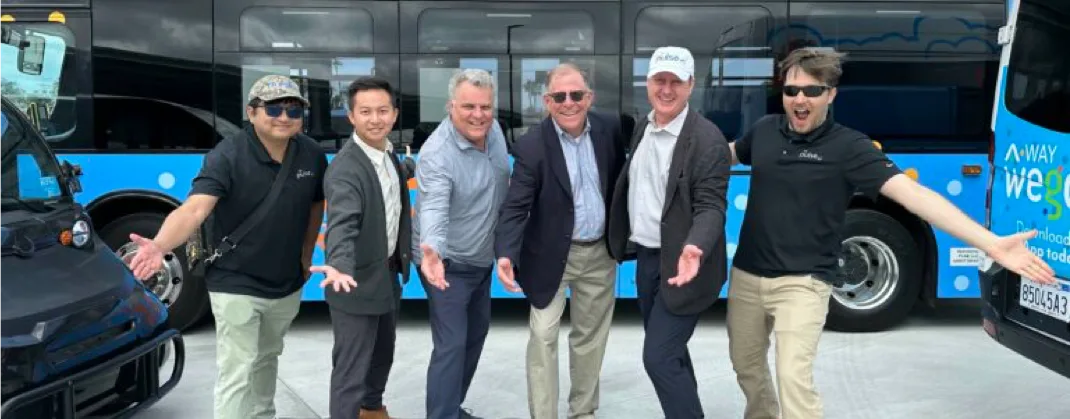 Six men standing next to some EVs looking happy and holding their arms out in celebration. 
