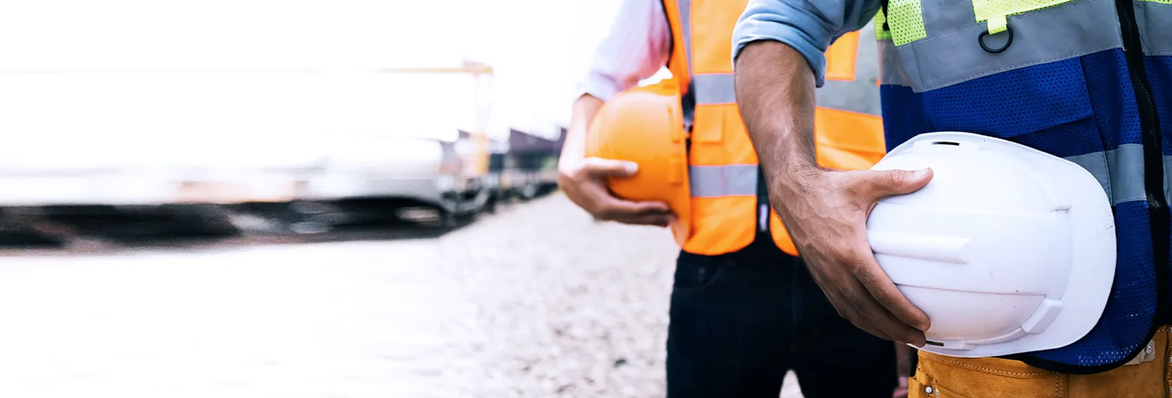 A close up of the torsos of two people in high vis jackets, holding hard hats.