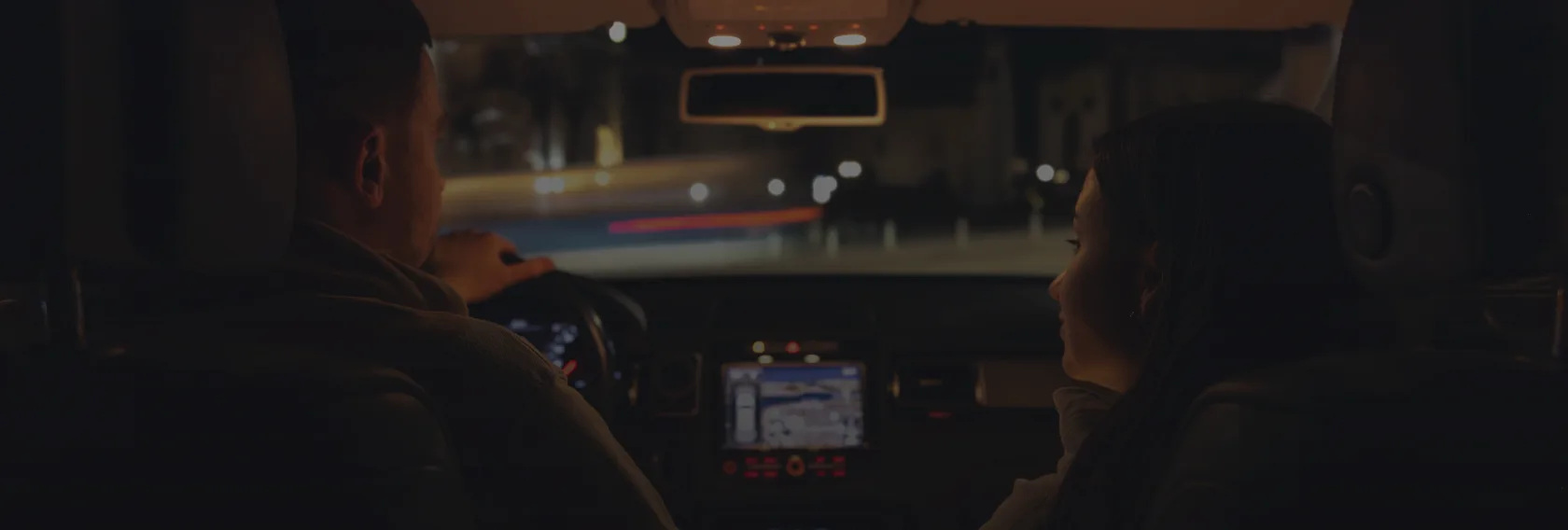 A father and daughter sit in the front seats of their car at night time.