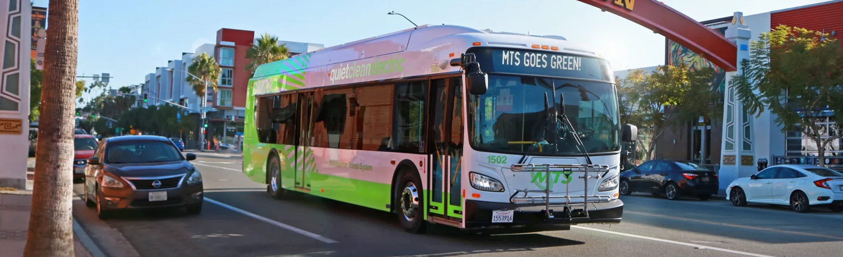 An electric bus drives down a San Diego street on a bright day. 