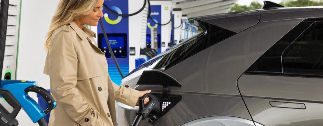 A woman using a bp pulse charger to charge her grey EV.