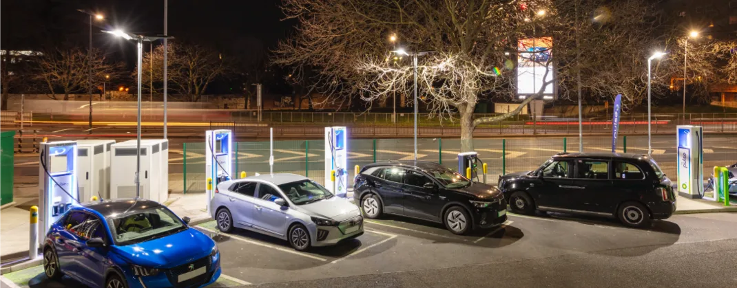 Four EVs charging on a dark evening, in a floodlit setting. 
