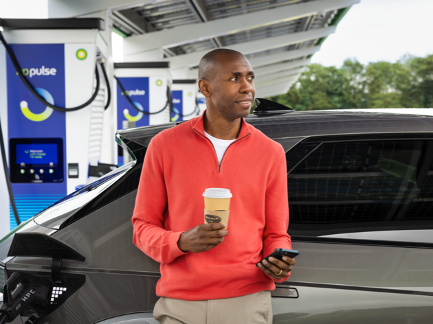 Man relaxing with a takeaway coffee while his car charges at a bp pulse charging station.