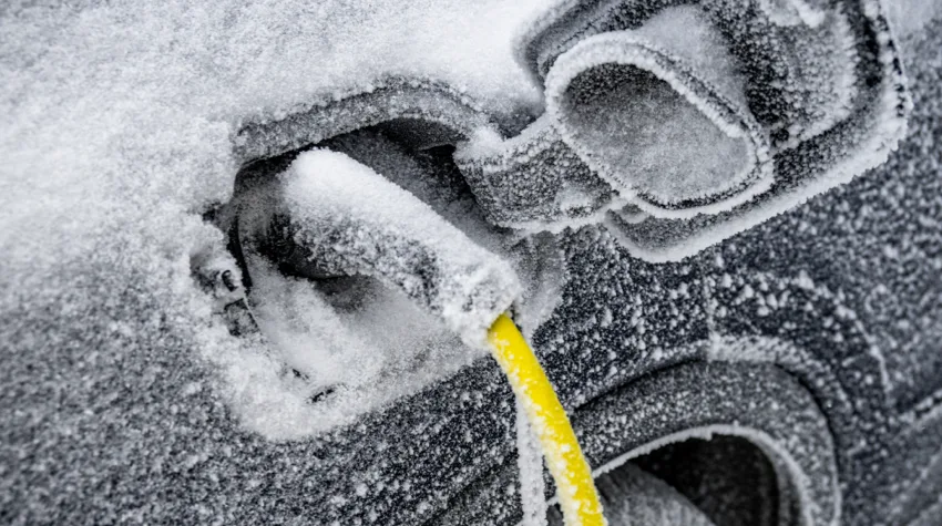 An electric charger plugged into a car covered in snow.