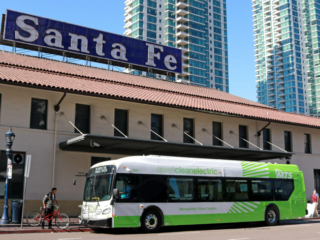 A green and white electric bus is parked outside a Santa Fe bus station.
