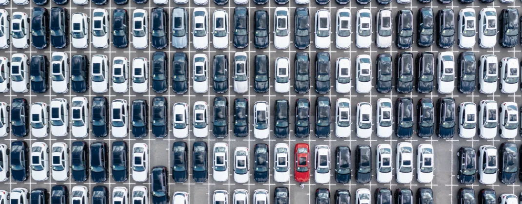 Lots of white, grey and black cars in a parking lot, all parked. 