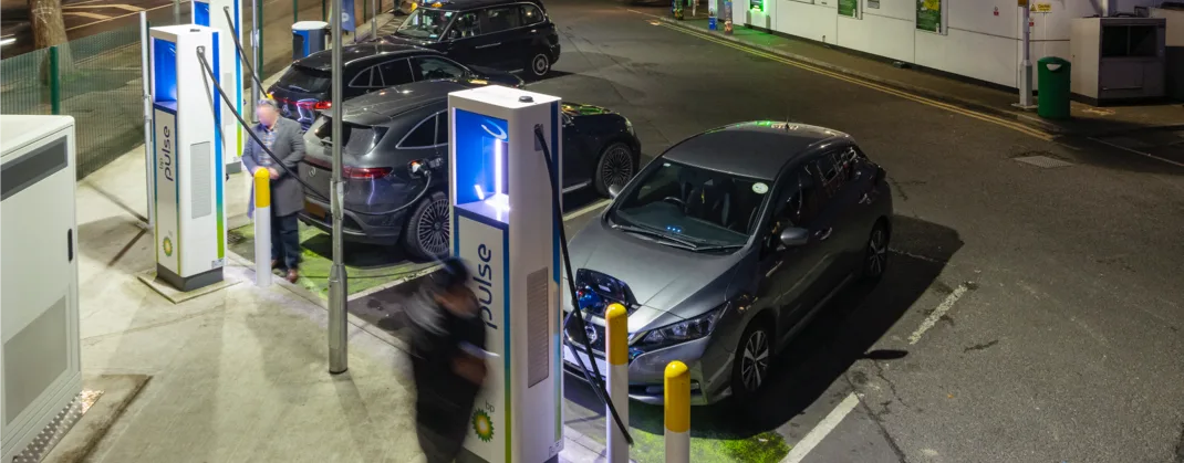 Electric vehicles charging at a well-lit bp pulse charging station late at night, ensuring visibility and safety in the dark.