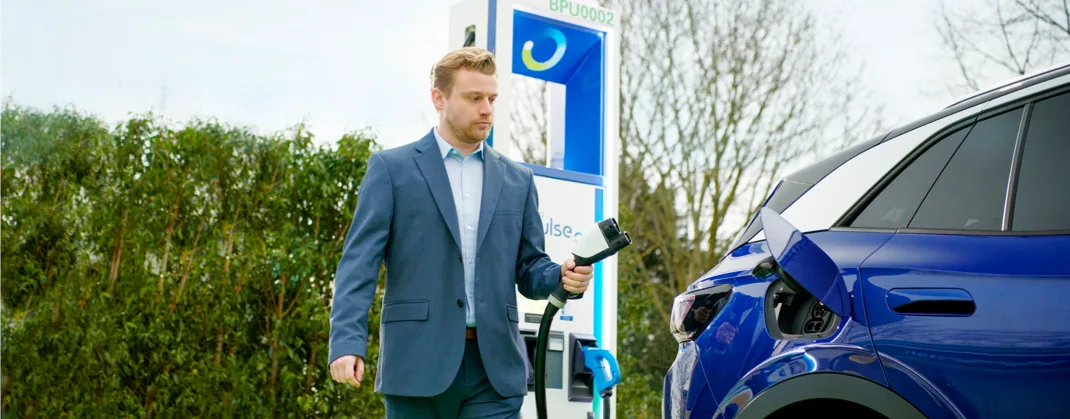 A man in a suit about to charge his blue EV from a bp pulse charger. 
