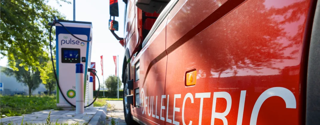 A bright colored electric truck is parked near a bp pulse charger on a sunny day.