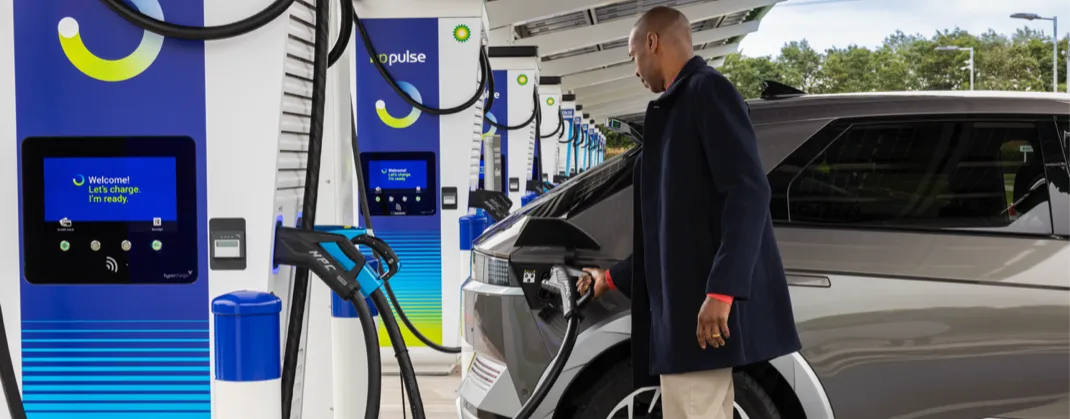 A person plugs in an electric vehicle at a bp pulse charging station, with multiple chargers in a well-lit, covered charging area.