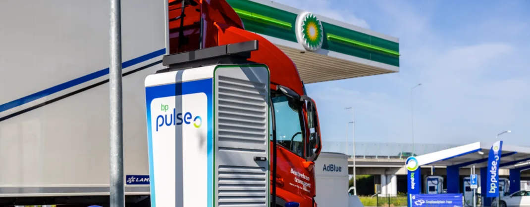 An electric transport truck is parked near a bp pulse charger.