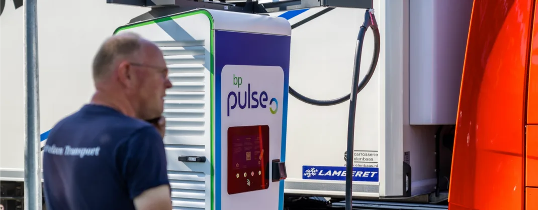 A bp pulse charging station in use, connected to a vehicle, with a person in the foreground and a truck in the background.