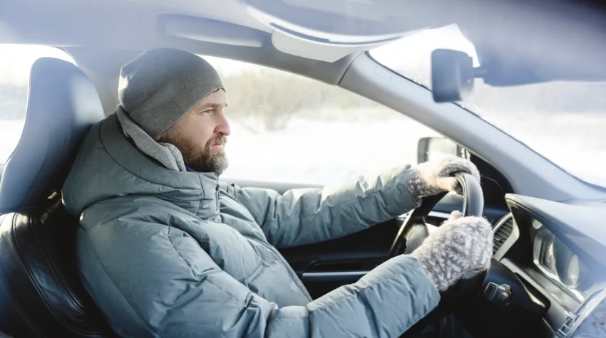 Person dressed in warm clothes driving a car.