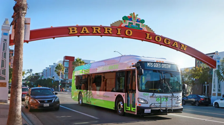 A bus driving under a red bridge, on a sunny day. 
