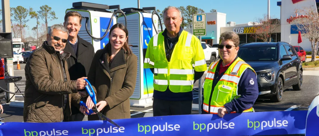 A ribbon cutting ceremony at the first Electric Vehicle charging hub at travelcenters of America. Three people are together cutting the blue ribbon with a large pair of blue scissors.