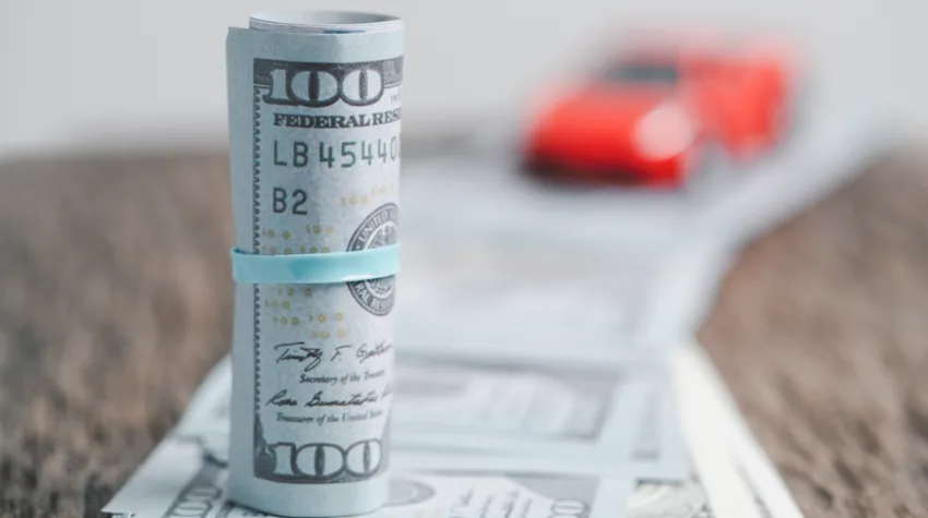 A currency note tied in a bundle and a toy car in the background, stacked over a line of currency notes, placed on a table.