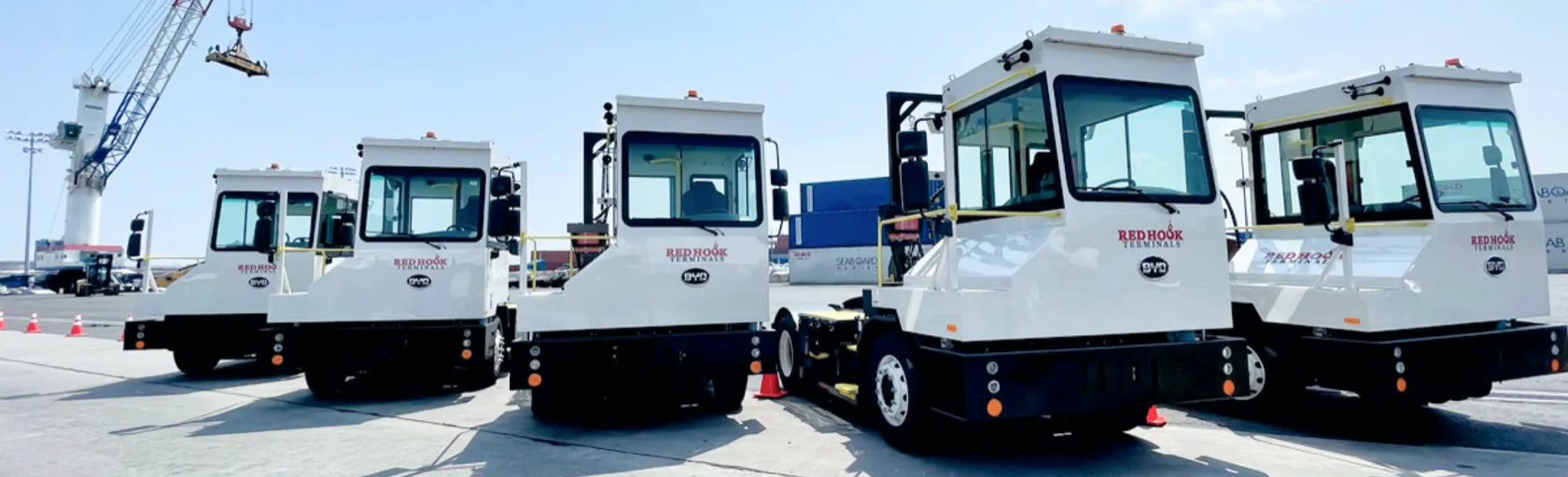 Five white Red Hook terminals are parked next to each other, shipping containers and a large crane is in the background.