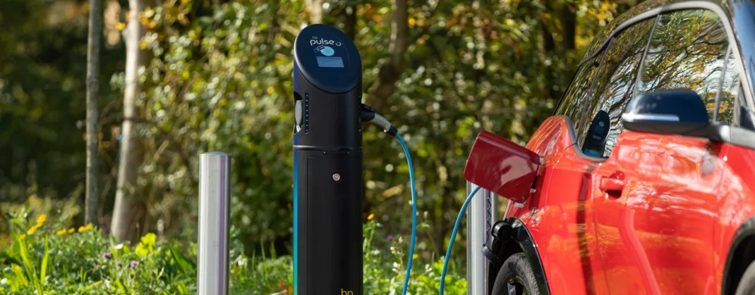 An electric vehicle charging at a bp pulse station set in a natural, green environment.
