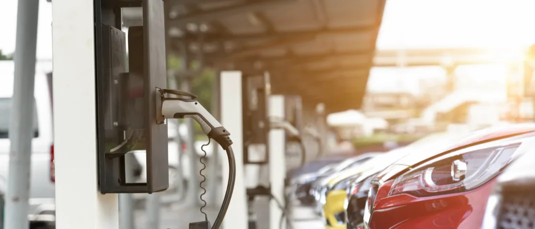 An EV charging station with electric vehicles parked in the charging bays infront of them. Only the the sidelights of the EVs are visible.