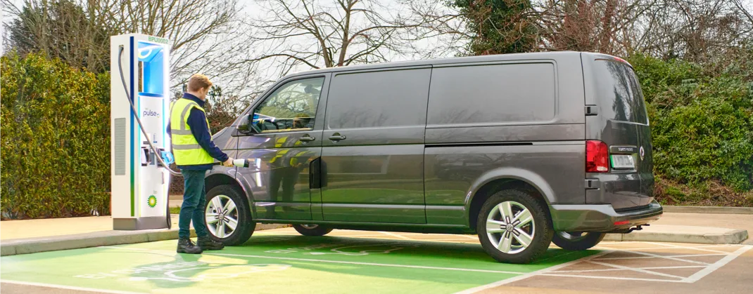 A technician holding a bp pulse EV charger and inspecting a parked black van. 