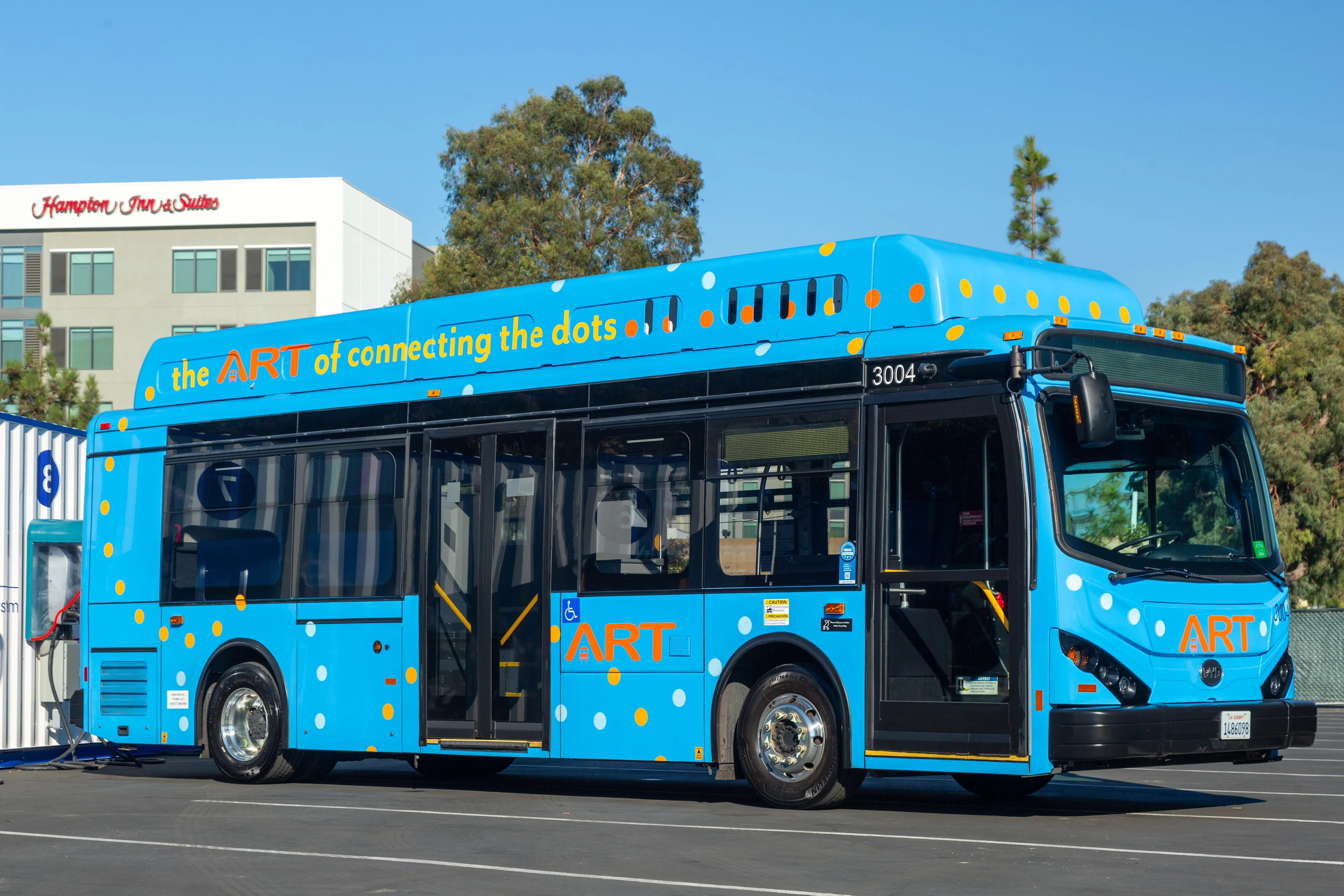 A blue Anaheim Transportation Network branded electric bus parked up on a bright day.