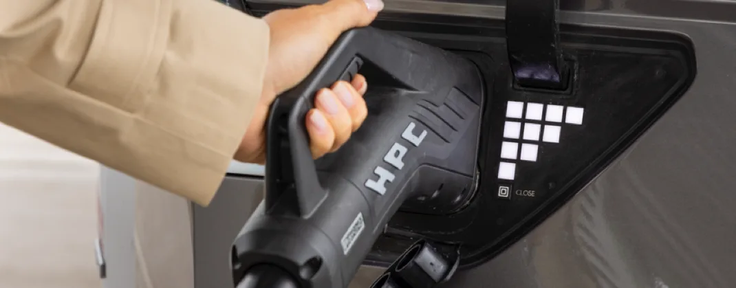 A female hand holding a black ev charger within her car. 