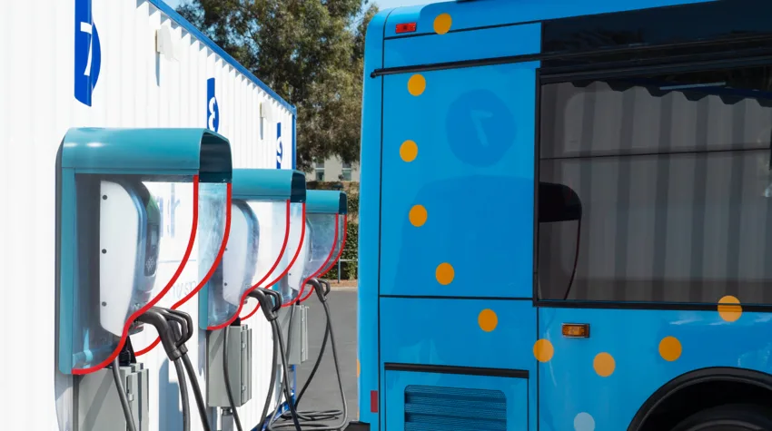 A blue bus by some charging points with red and black cables. 