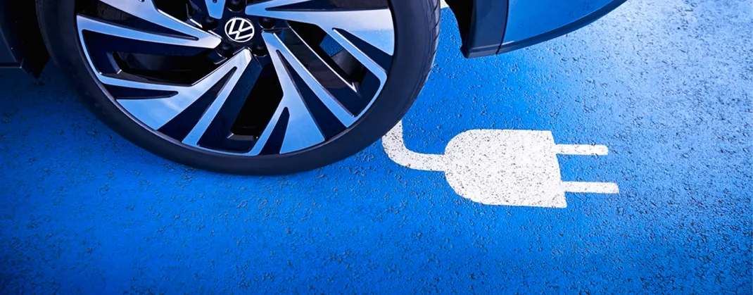 Close-up of a Volkswagen electric vehicle wheel parked over a blue charging bay marked with a white electric plug symbol.