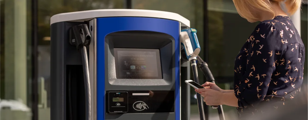 A woman uses the bp pulse app on her mobile phone to pay for charging at a bp pulse charger.