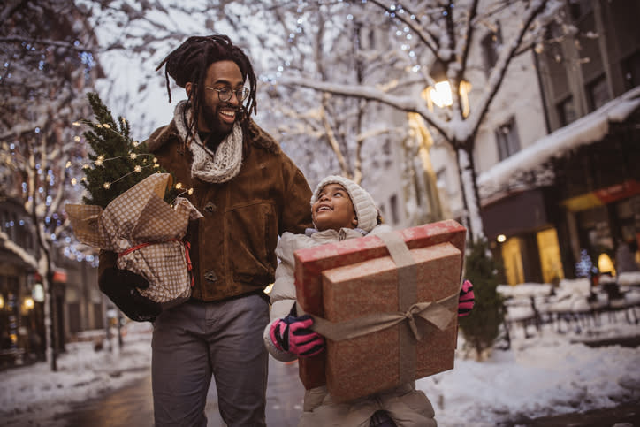 Man, and kid walking in snow road, holding some gifts