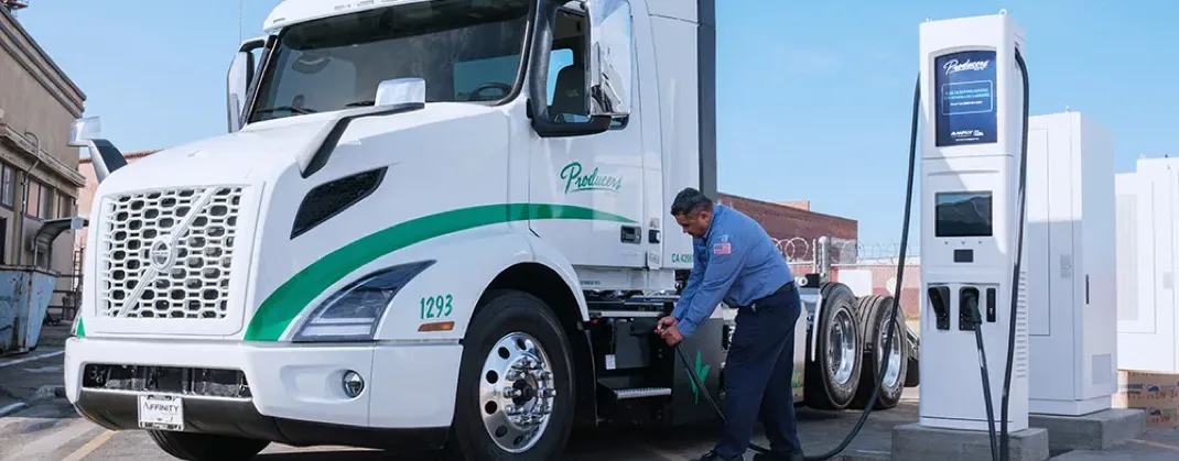A man in a uniform charging a Volvo VNR electric truck deployed in California’s Central Valley.