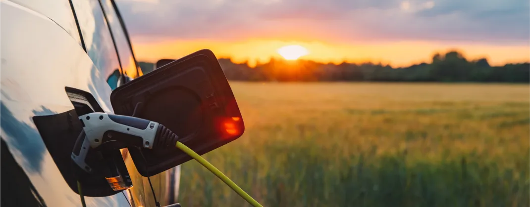 An EV is being charged while the sun sets in the background of an open green field.