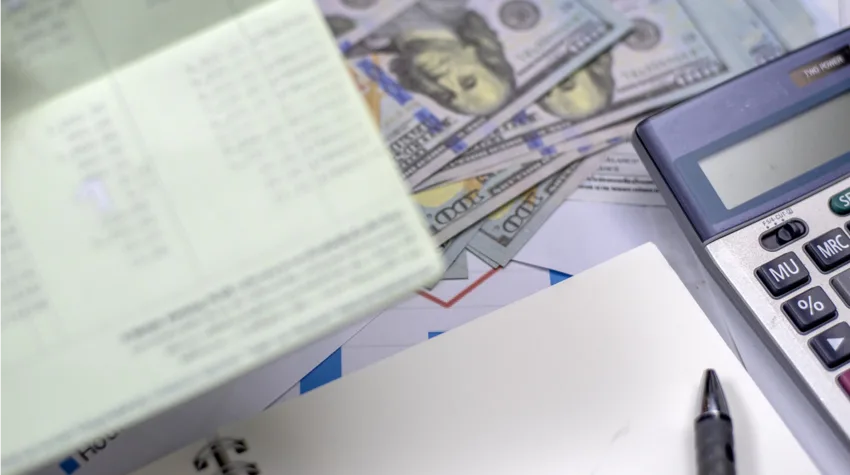 Paper, pen, calculator, and currency notes spread across a table.