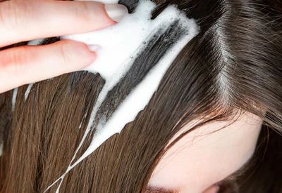 Close up of the top of a woman’s head with long brown hair applying woman’s Rogaine Foam. Close up of the top of a woman’s head with long brown hair applying woman’s Rogaine Foam.