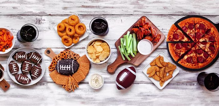 Top down view on a white wood background of pizza, hamburgers, wings, snacks and sides.