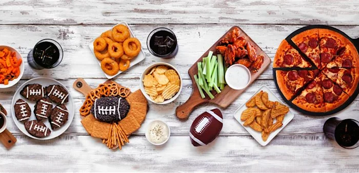 Top down view on a white wood background of pizza, hamburgers, wings, snacks and sides.