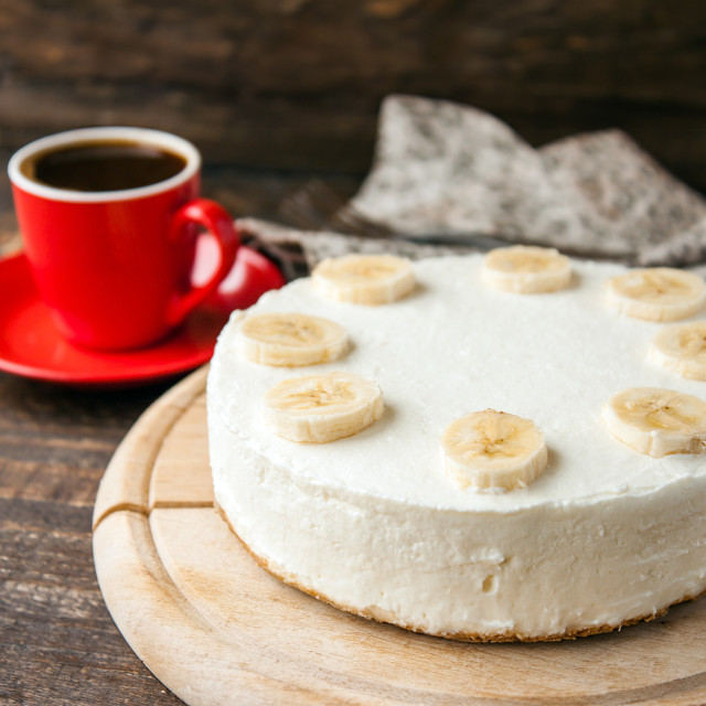 Banana coconut cake on wooden board with coffee in a red mug on the side