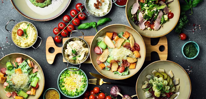 Plates of dishes for picnic including skewers, vegetables, fruits and drinks.
