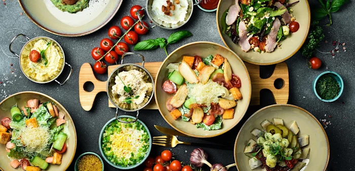 Plates of dishes for picnic including skewers, vegetables, fruits and drinks.