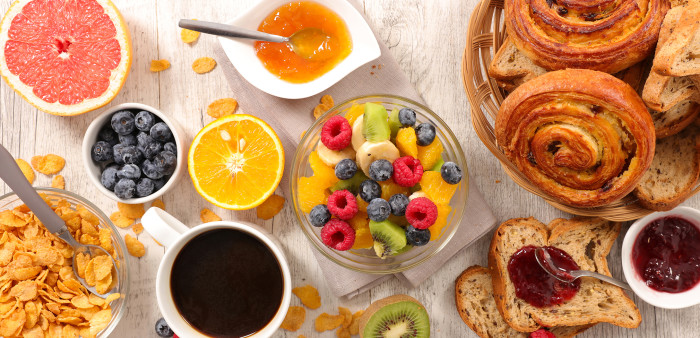 A selection of various breakfast foods, including cinnamon buns, coffee, fresh fruit and cereal