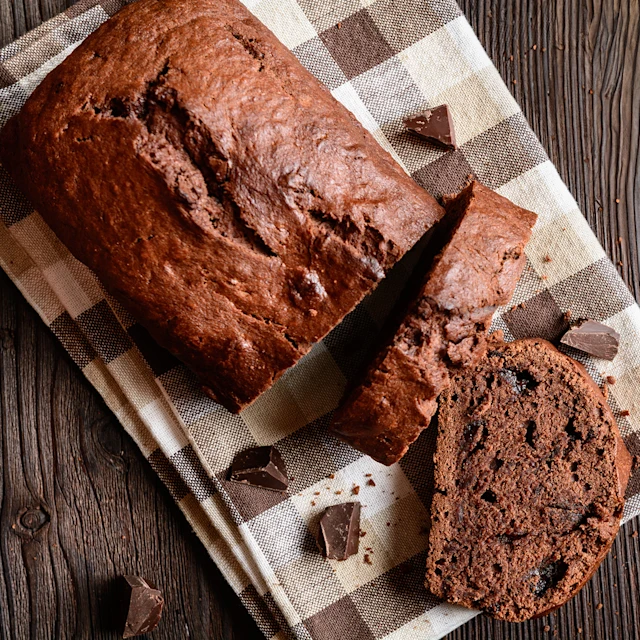 A partially sliced loaf of chocolate banana buttermilk cake on a tea towel